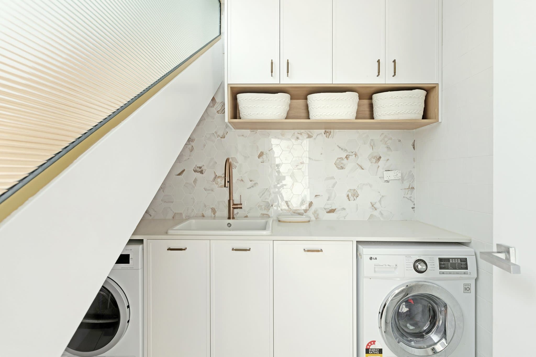 KBLCO laundry renovation, Sydney. White joinery, marble hexagon splashback and brass tapware.