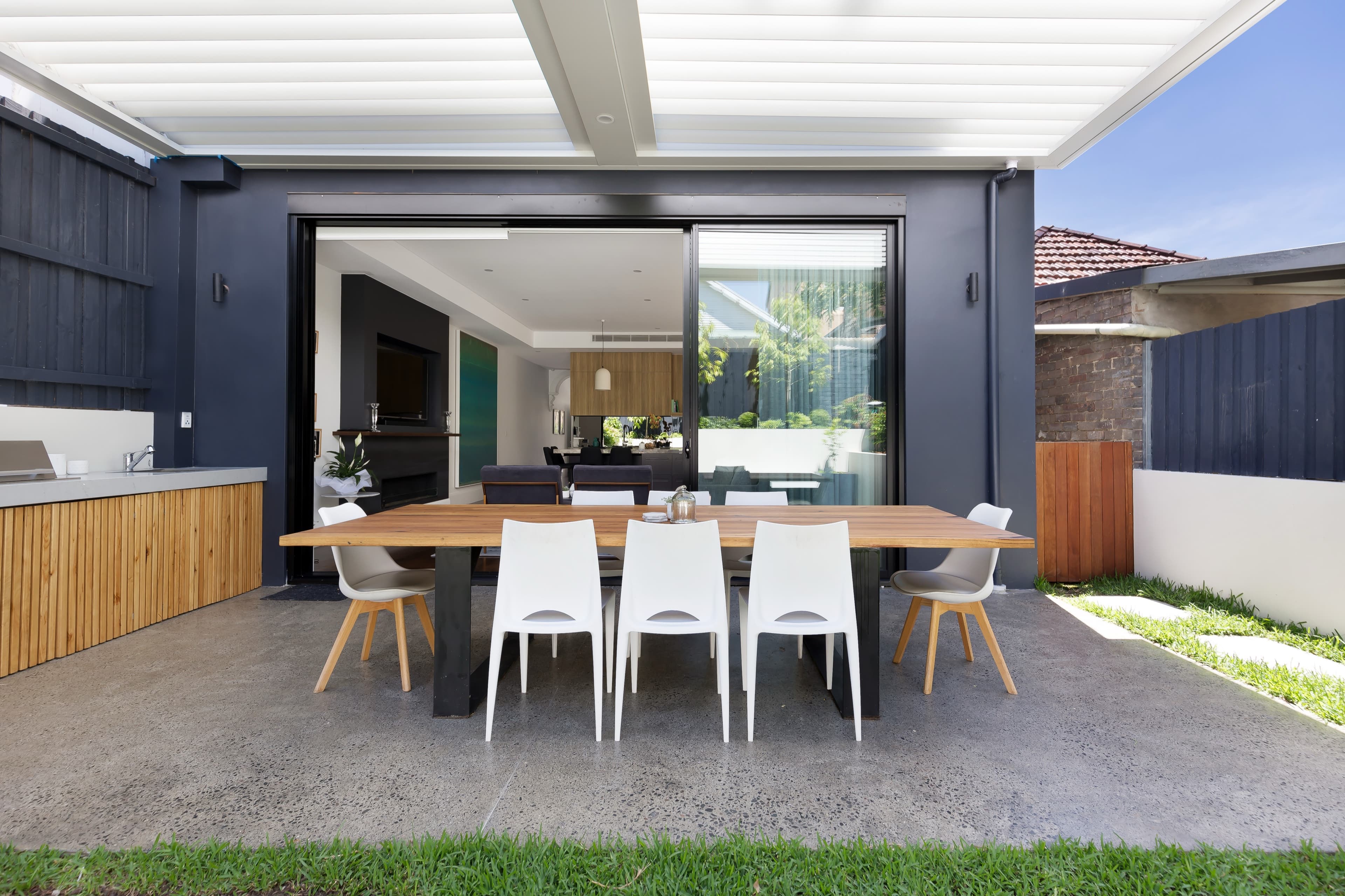 KBLCO living room, Sydney. Dining zone with white chairs and a garden outlook.